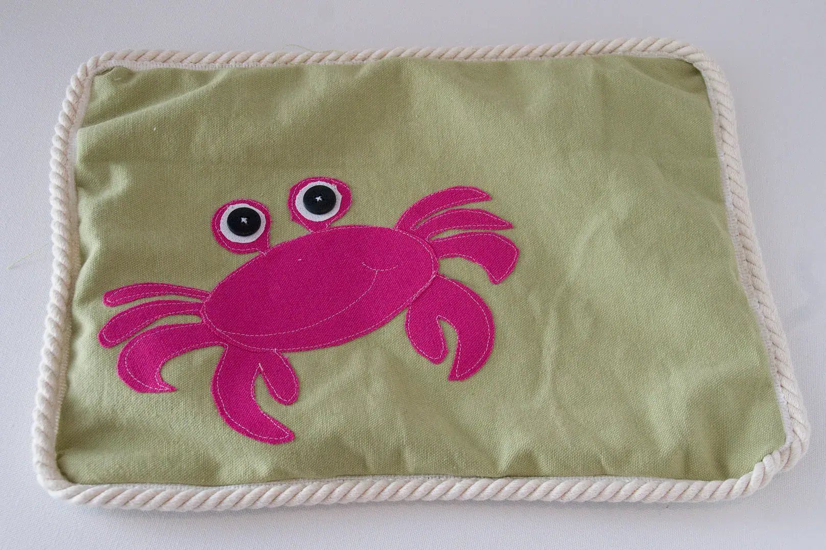 Three pillows on an outdoor couch, blue, green and green with a pink crab