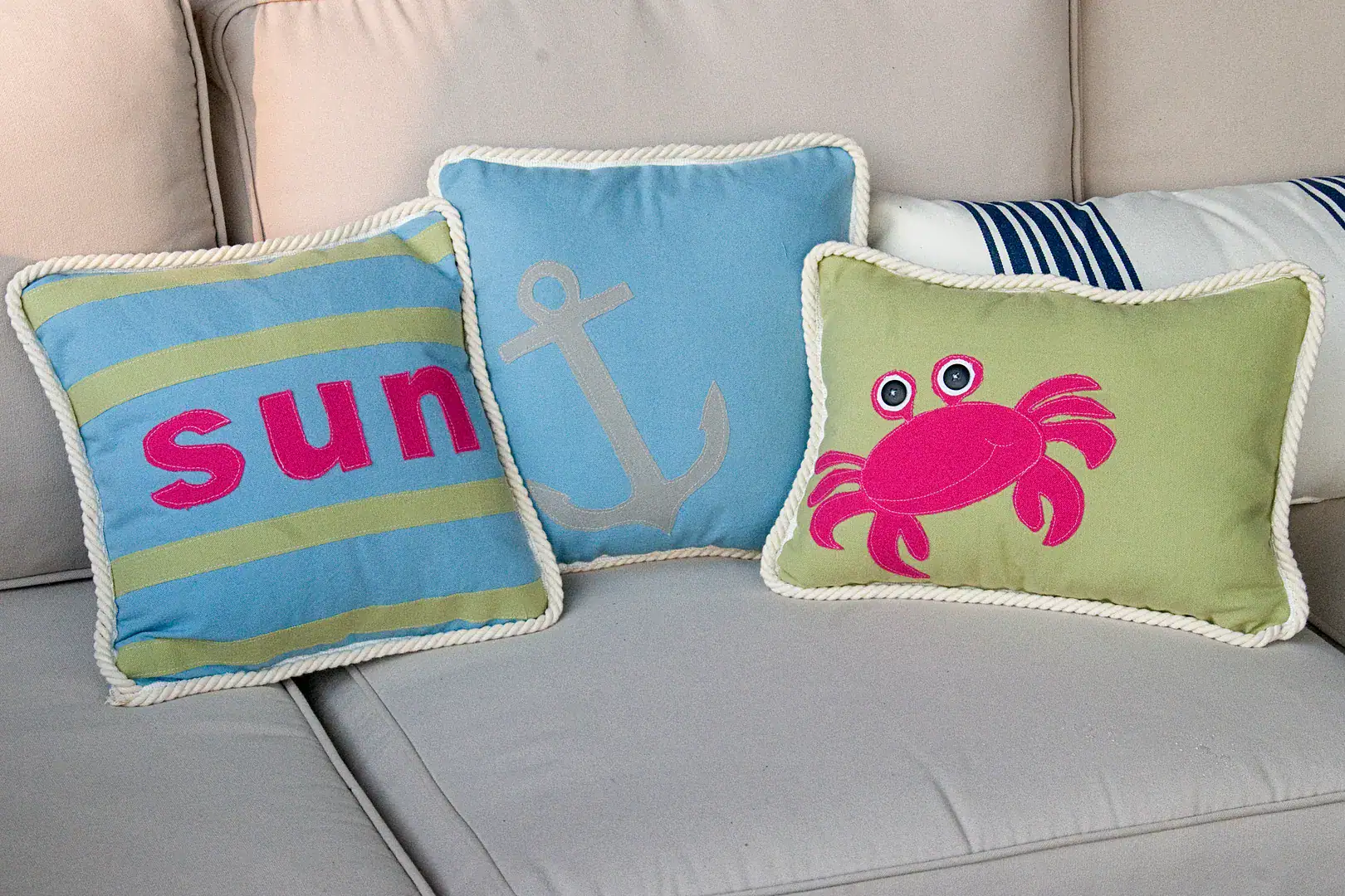 Three pillows on an outdoor couch, blue, green and green with a pink crab