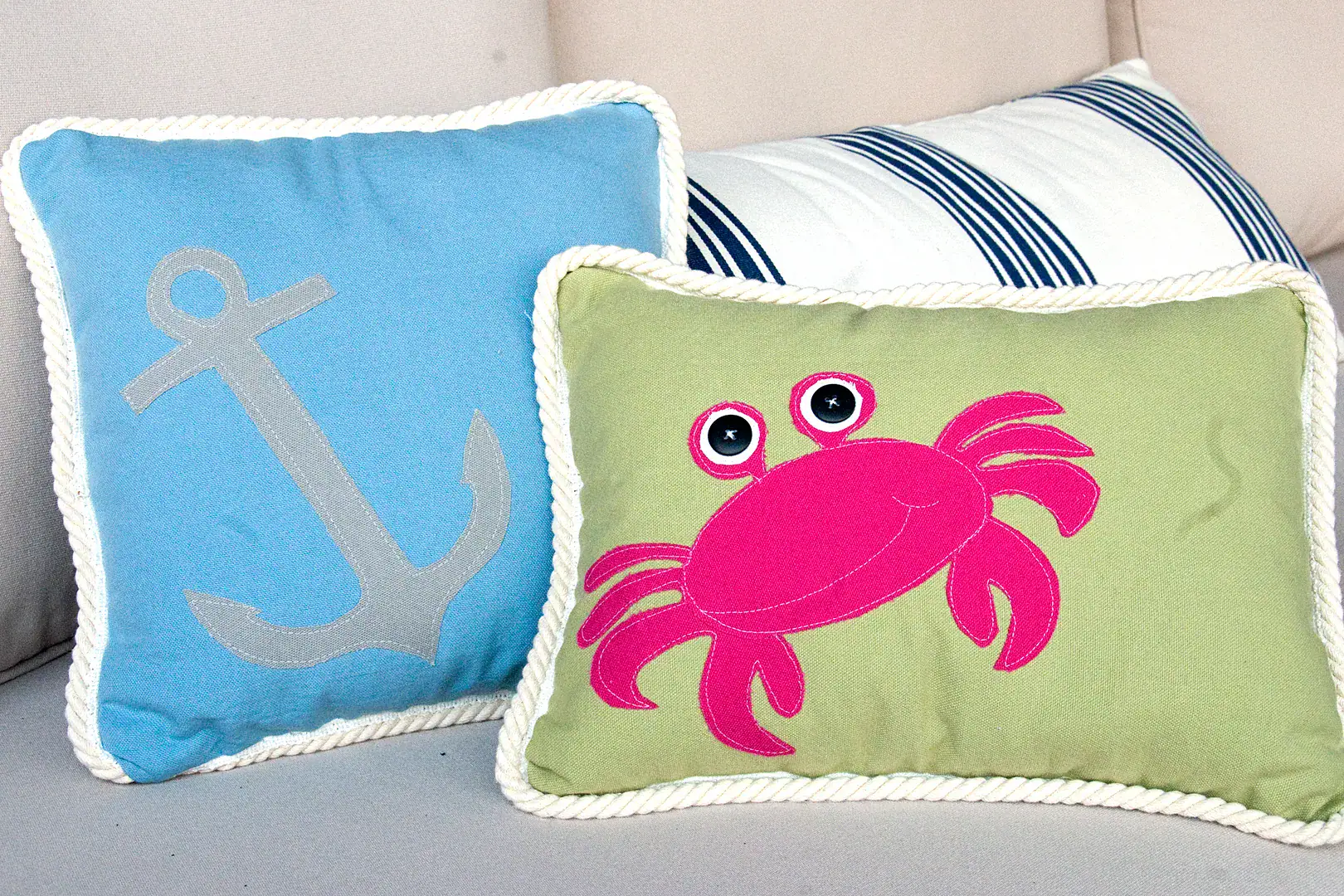 Three pillows on an outdoor couch, blue, green and green with a pink crab