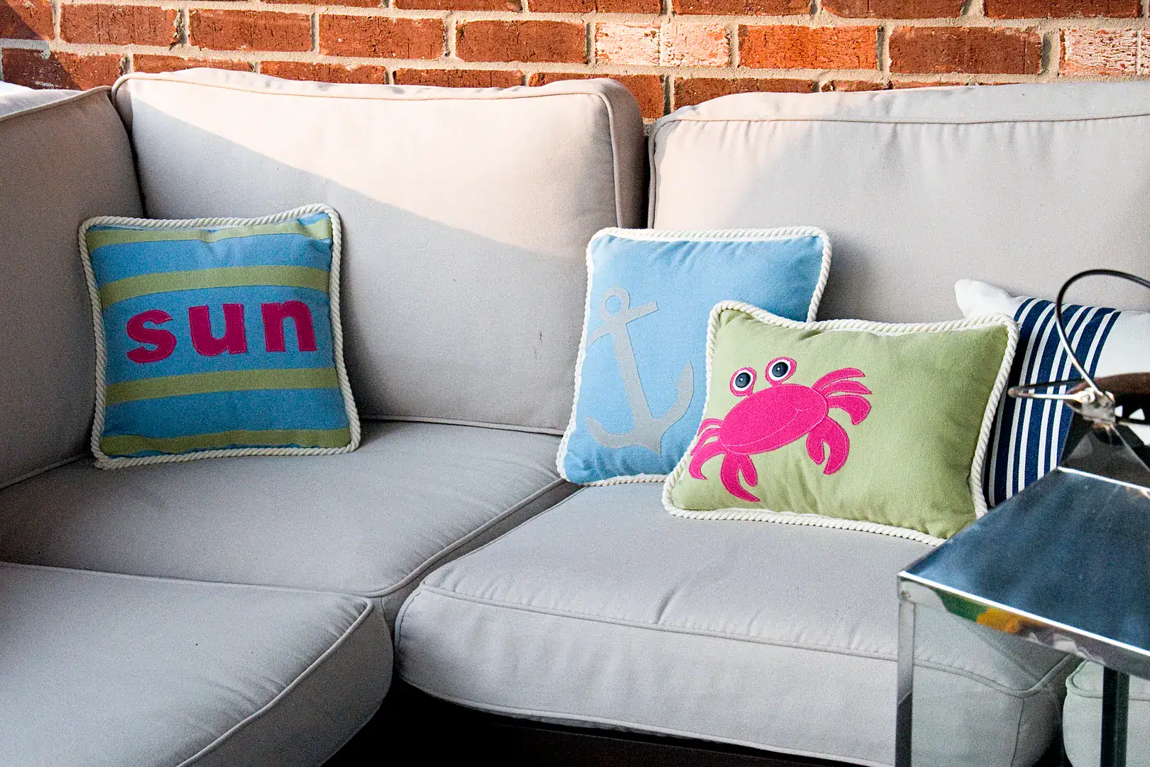 Three pillows on an outdoor couch, blue, green and green with a pink crab