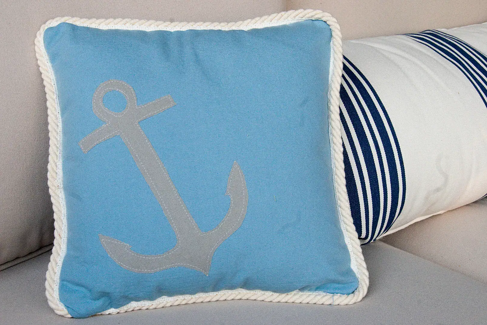 Three pillows on an outdoor couch, blue, green and green with a pink crab