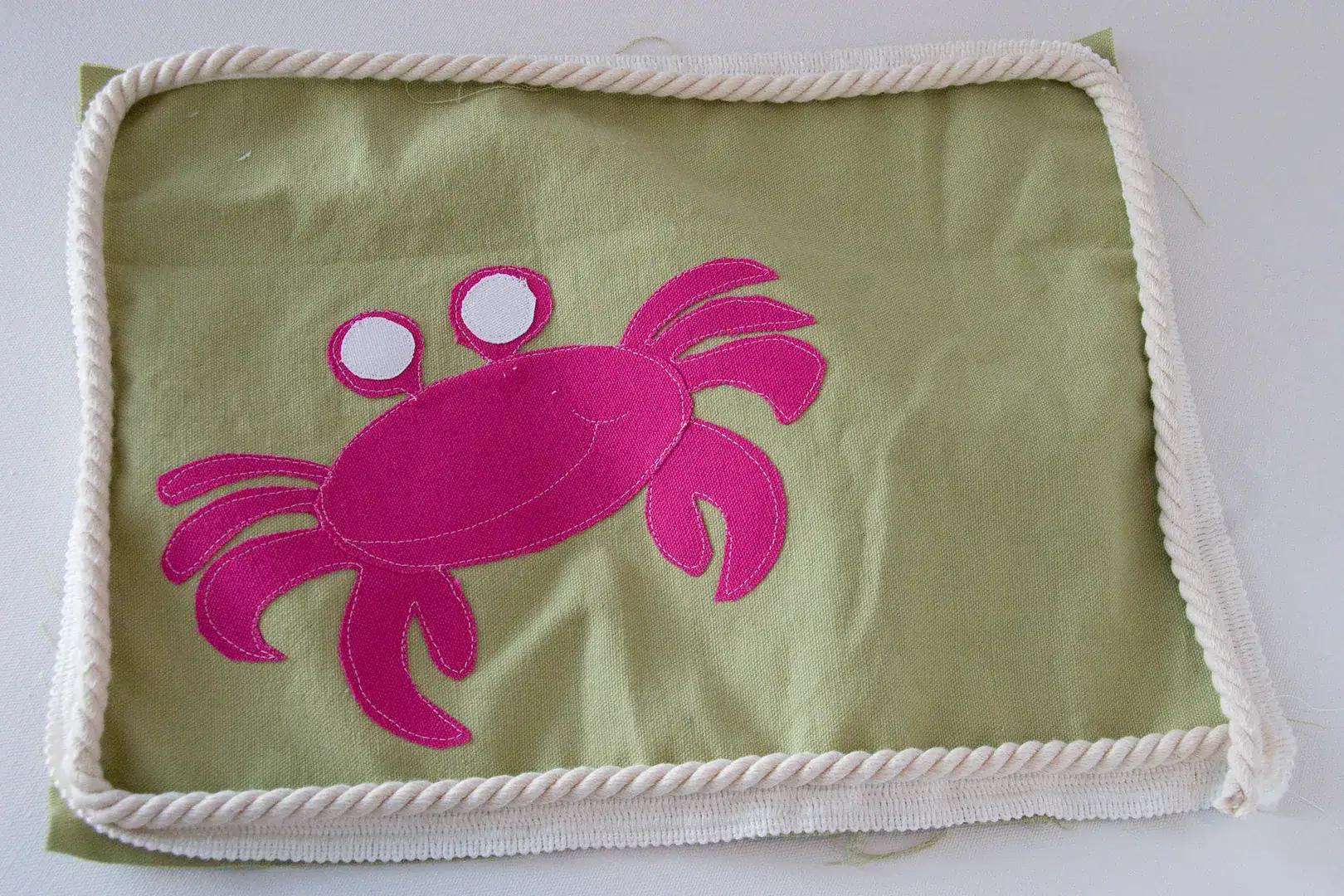 Three pillows on an outdoor couch, blue, green and green with a pink crab