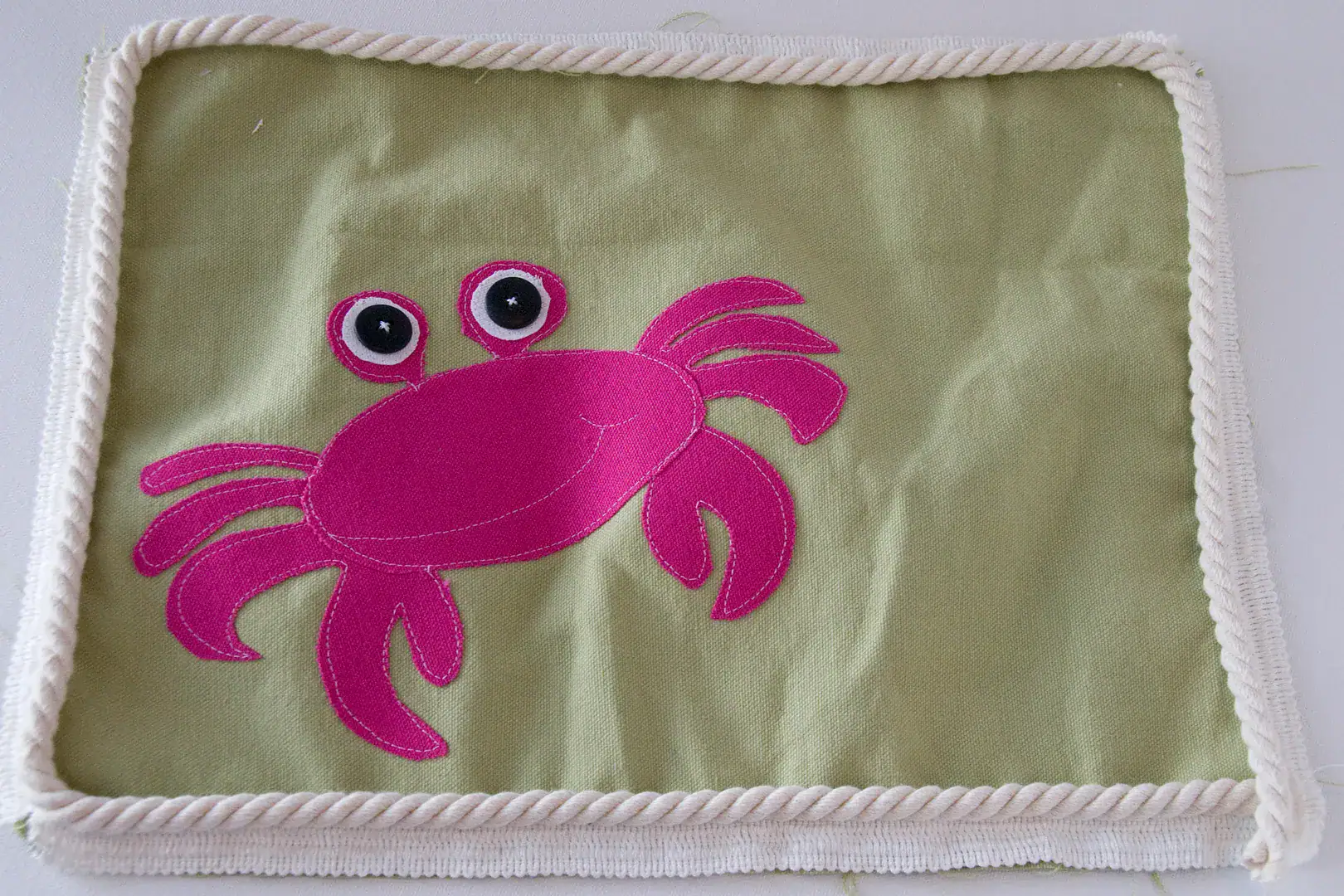 Three pillows on an outdoor couch, blue, green and green with a pink crab