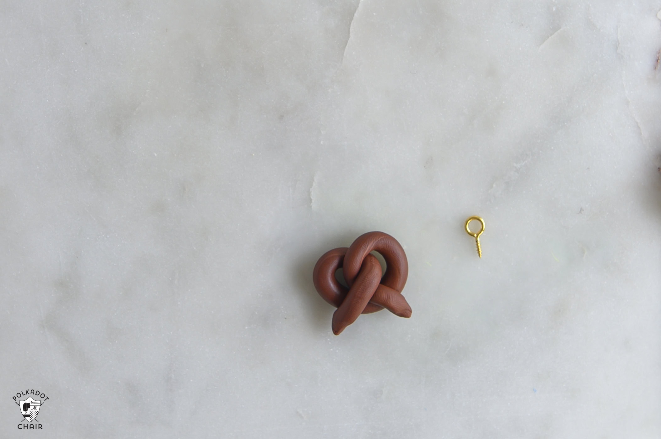 brown clay pretzel and gold screw with loop.