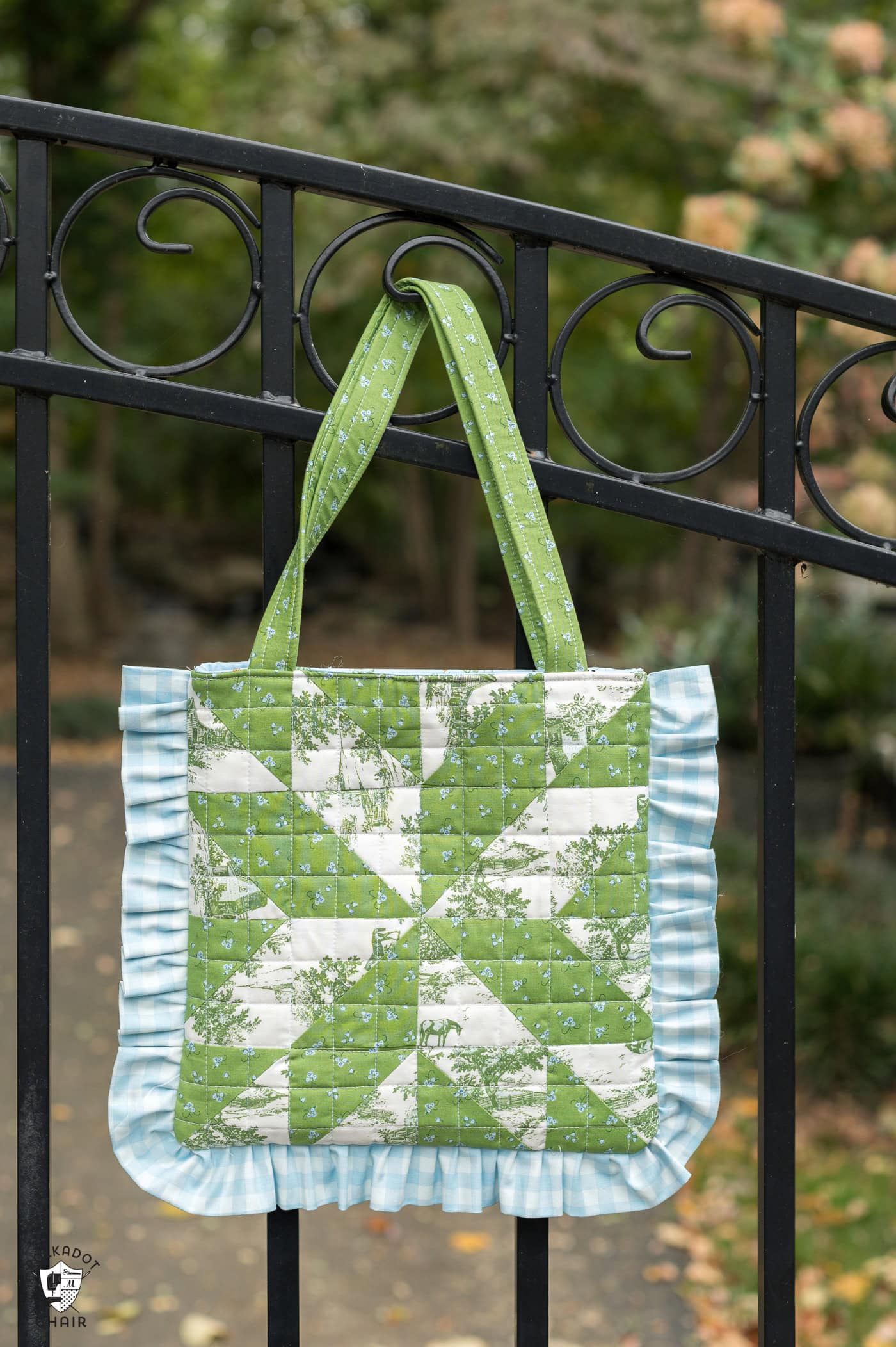 green and blue quilted tote bag hanging on metal fence