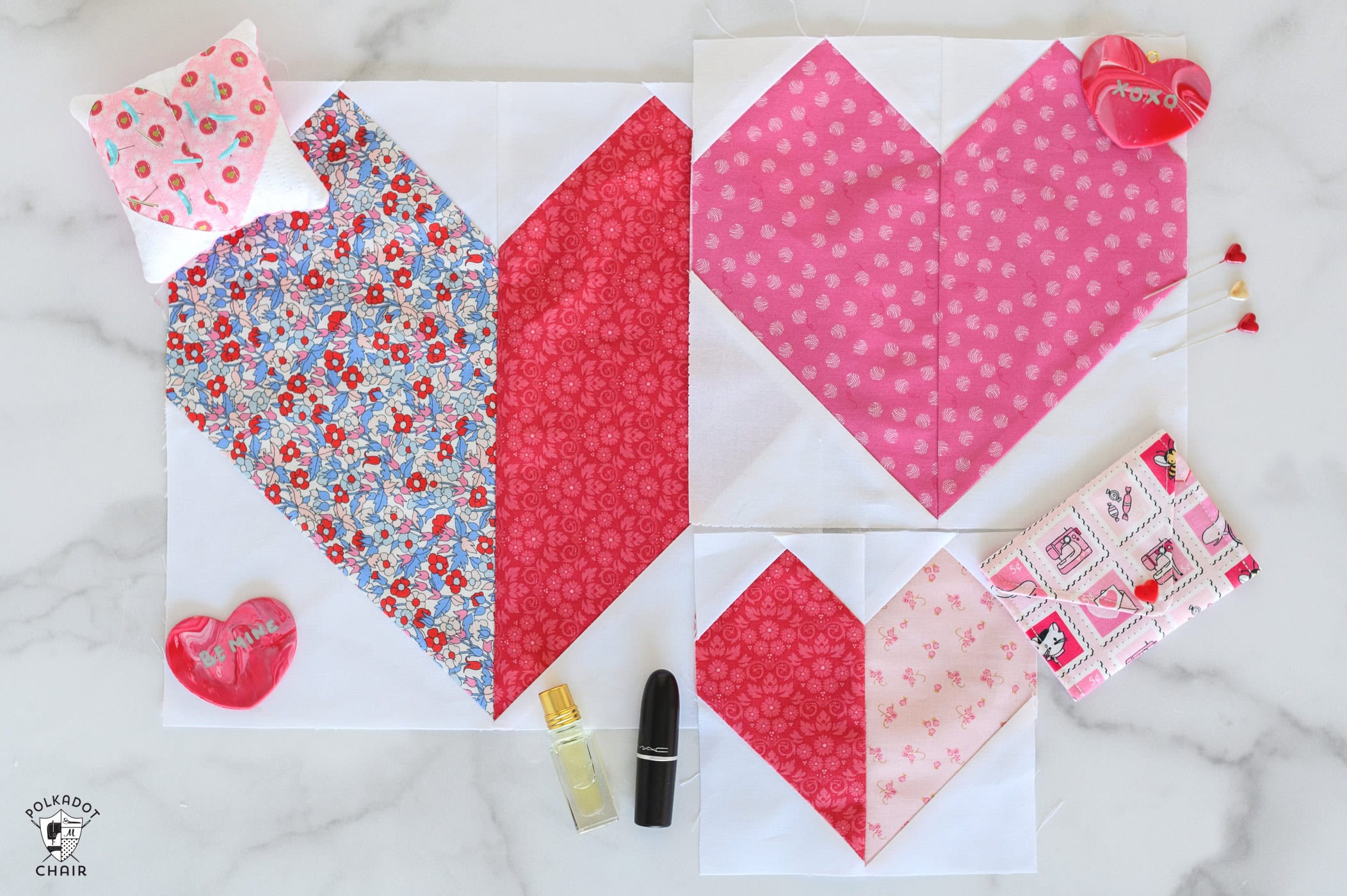 Three heart quilt blocks in pink, red and white on white table with sewing notions