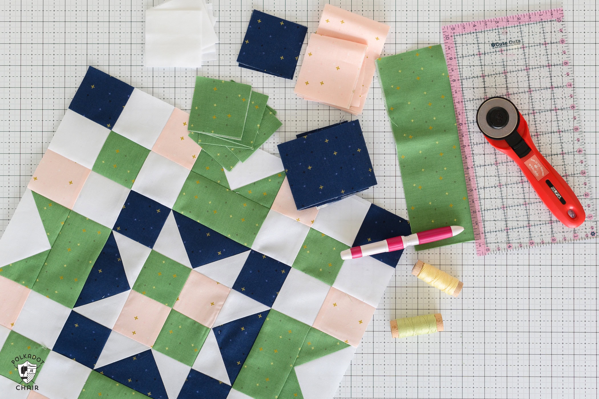 Green, navy, pink and white quilt block and fabric and quilt notions on white cutting mat
