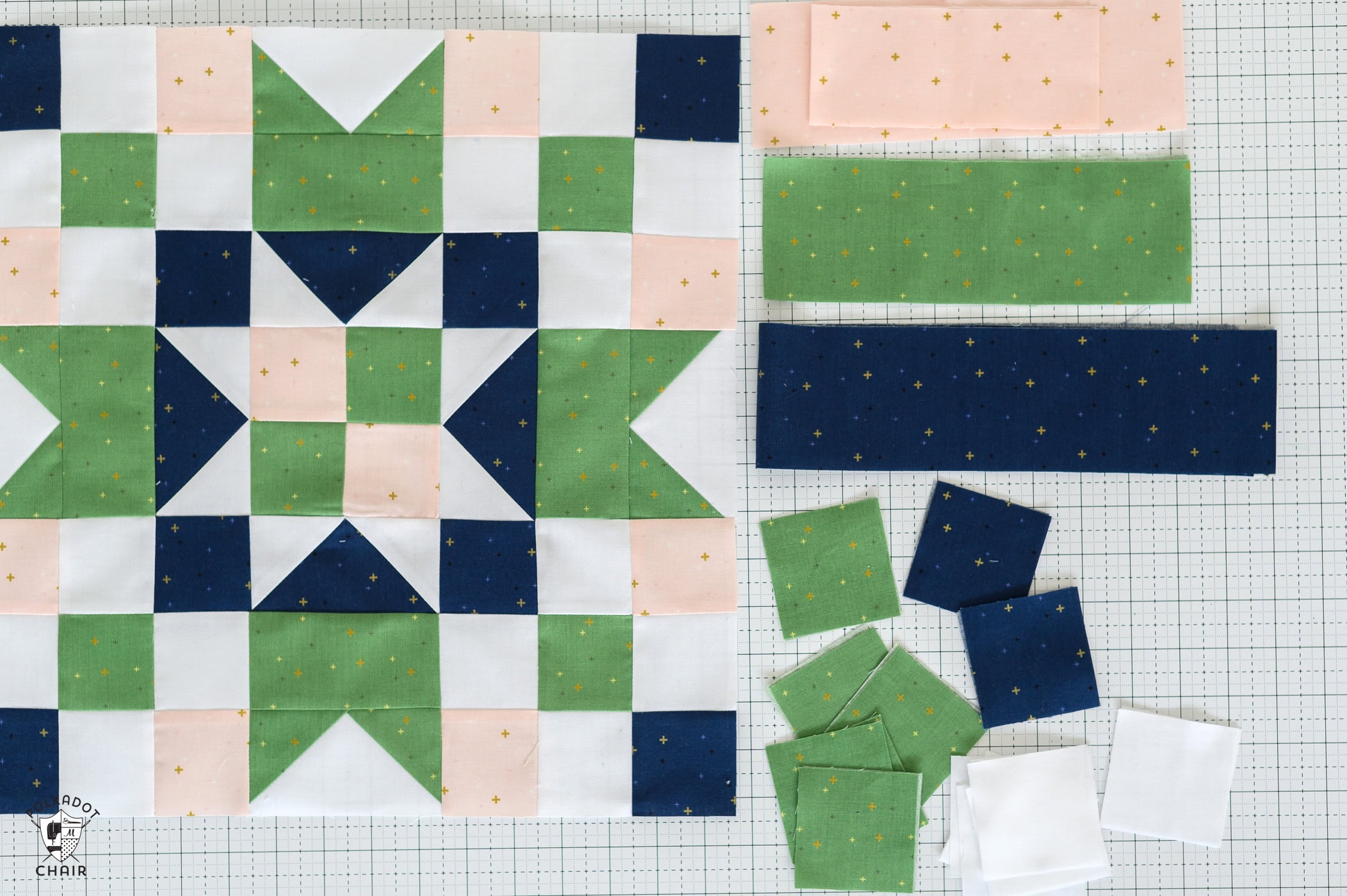 Green, navy, pink and white quilt block and fabric and quilt notions on white cutting mat