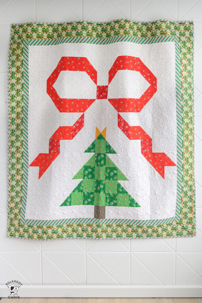 christmas quilt with large red bow and pieced christmas tree on white wall