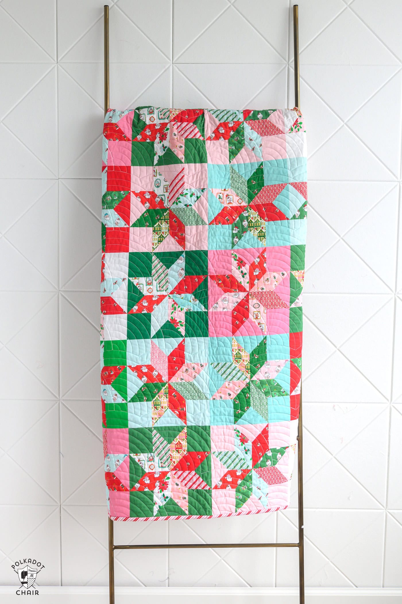 pink, red, green and white star christmas quilt on quilt ladder in front of white wall