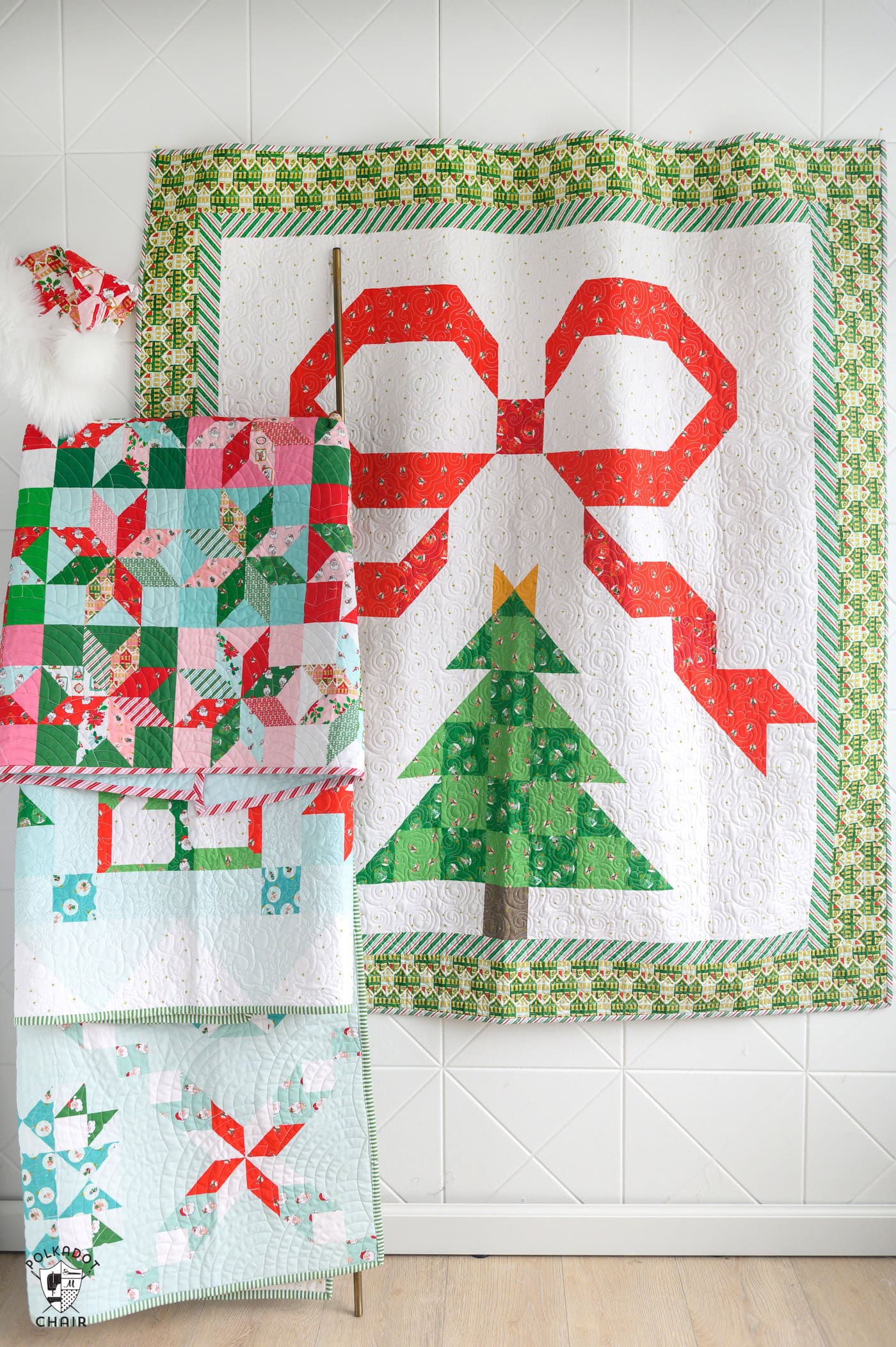 four christmas quilts on white wall, three on quilt ladder and one pinned to wall