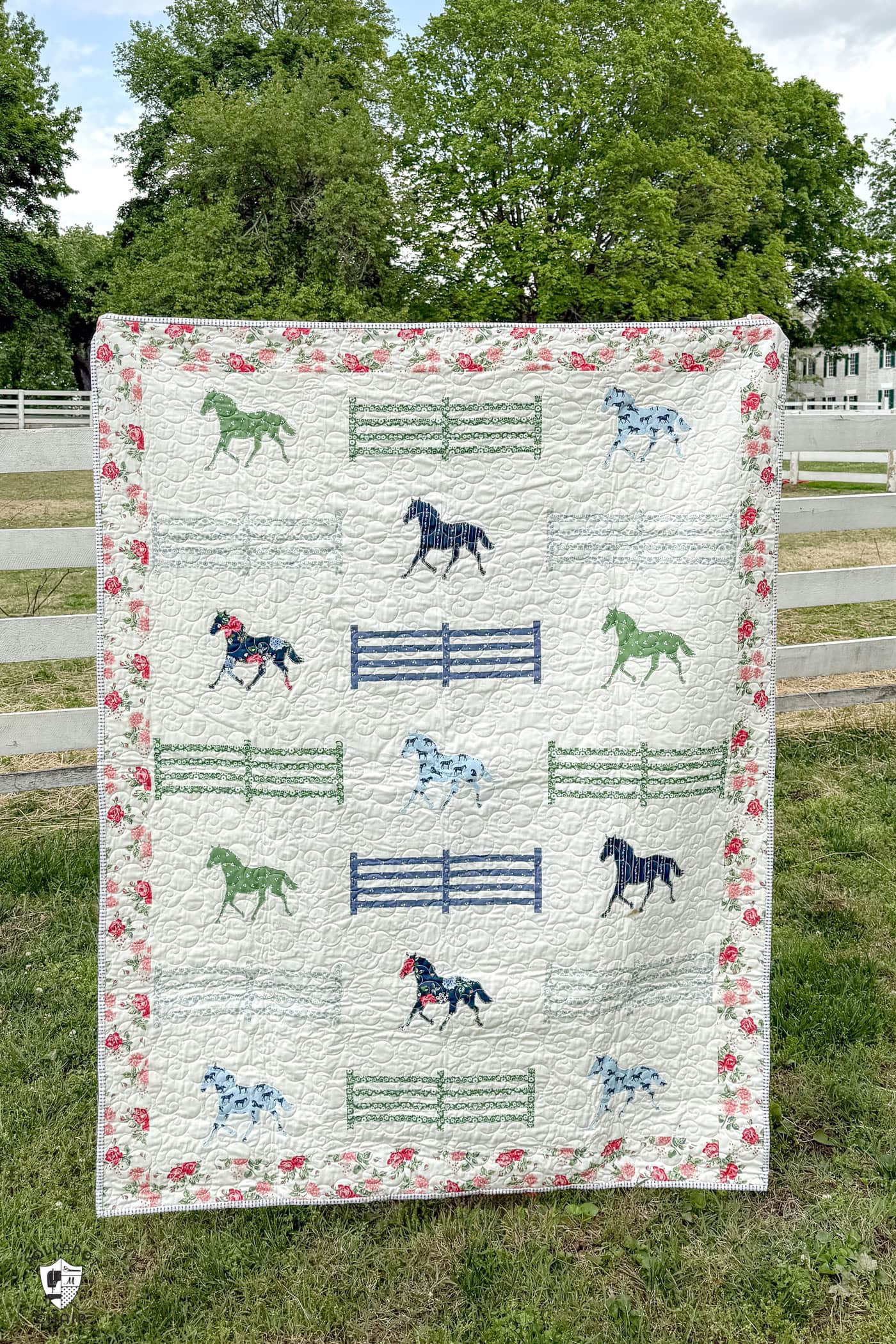horse quilt hanging on white horse fence in front of field