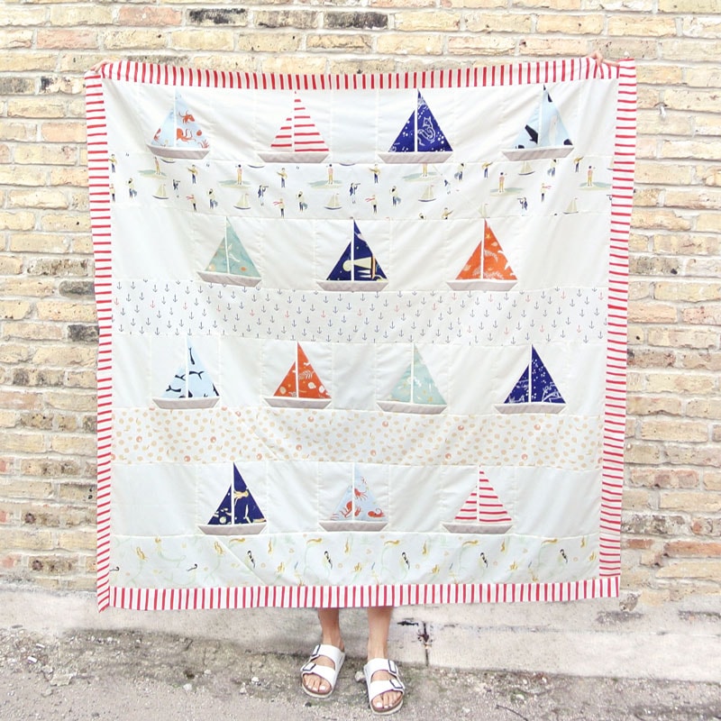 person holding sailboat quilt in front of brick wall