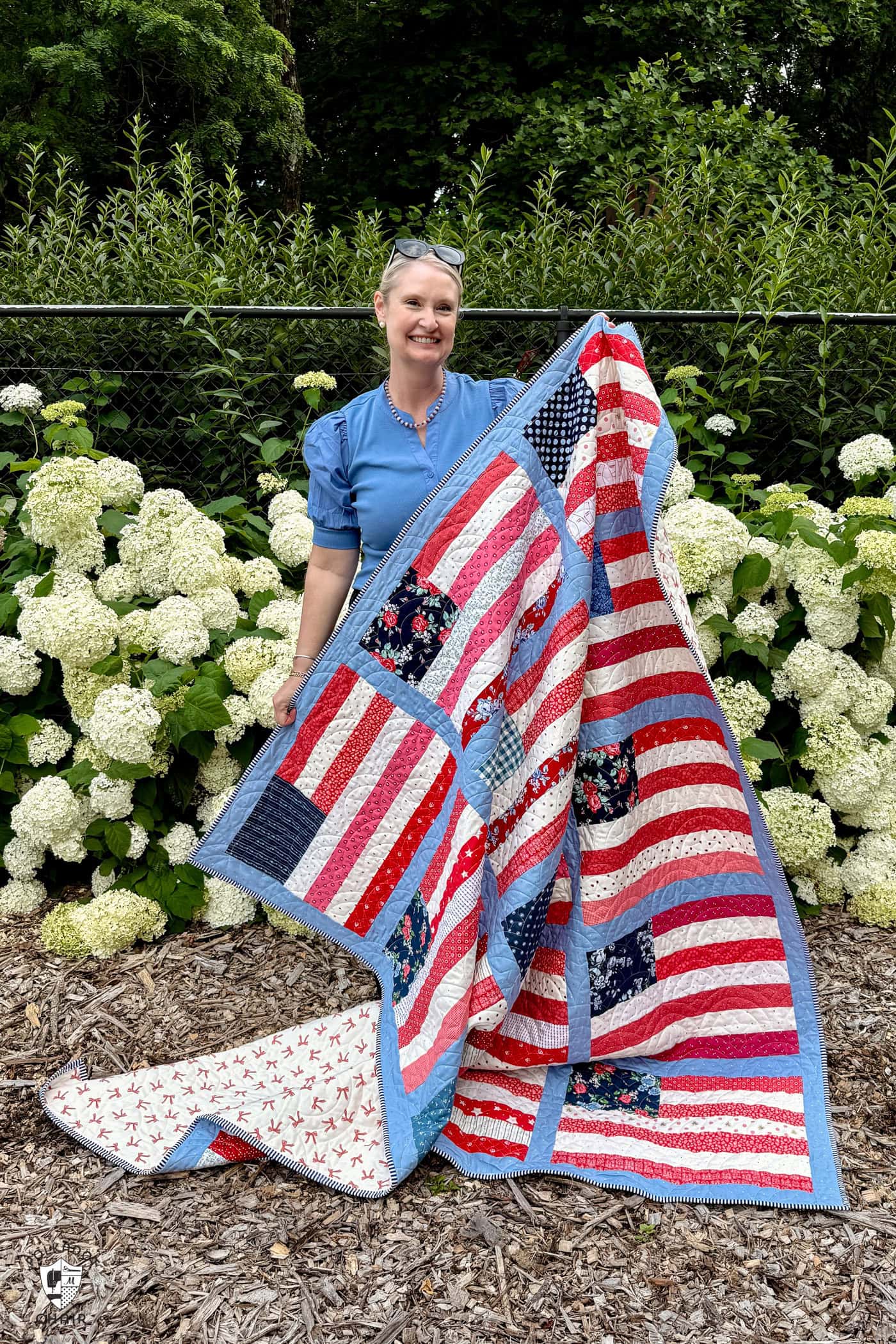 woman holding red white and blue american flag quilt in front of hydrangeas