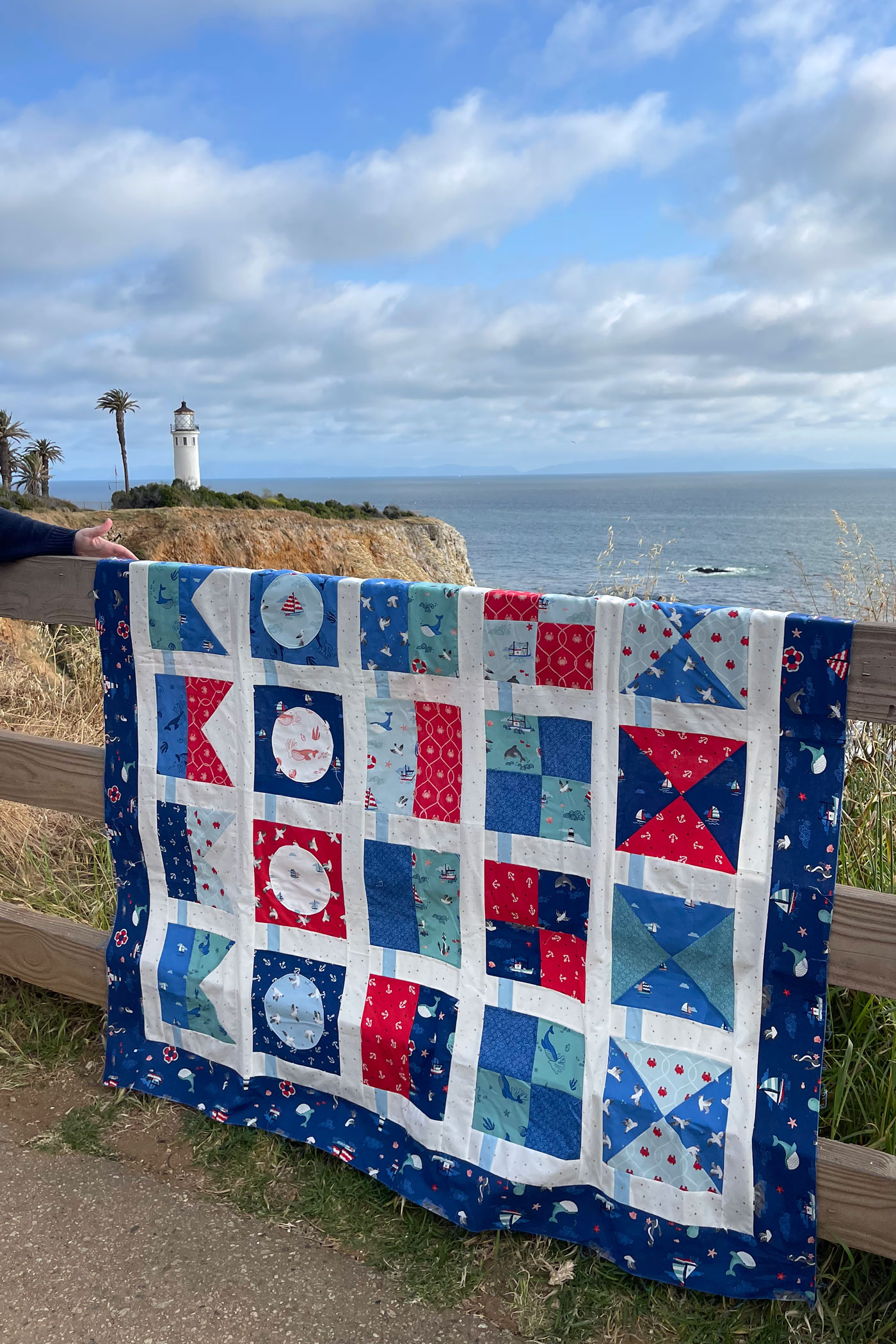 red, white and blue nautical quilt hanging on fence by lighthouse