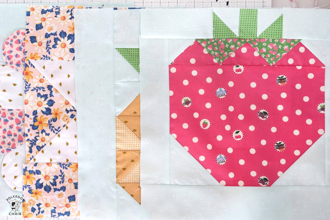 strawberry quilt block on top of other colorful fruit quilt blocks on table