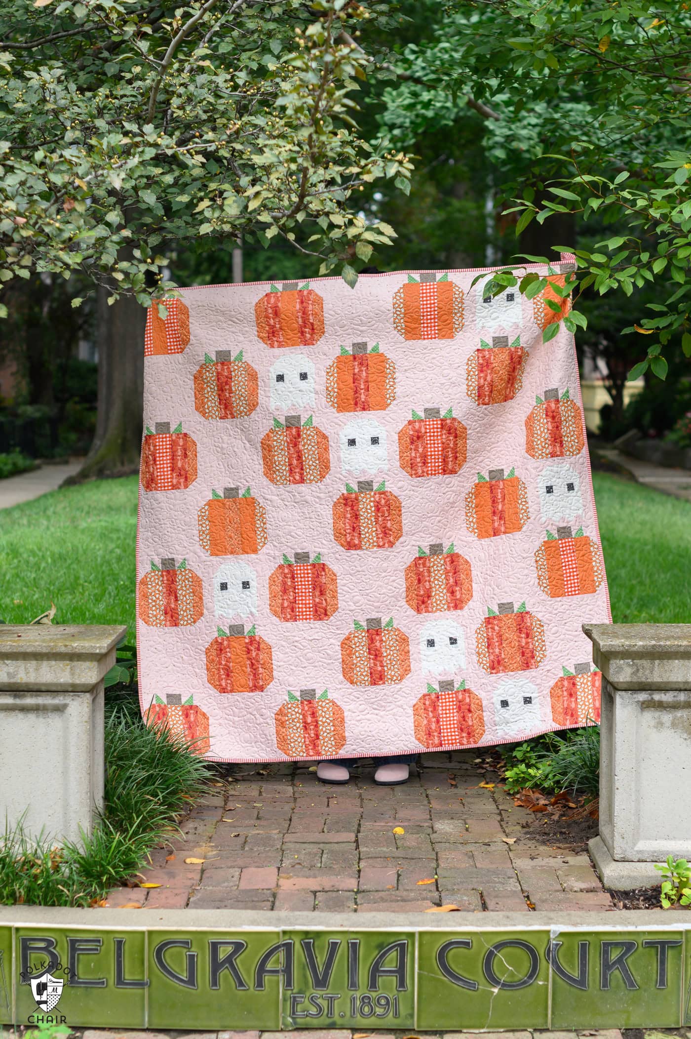 Pumpkin-themed quilt hanging outdoors in a garden setting.