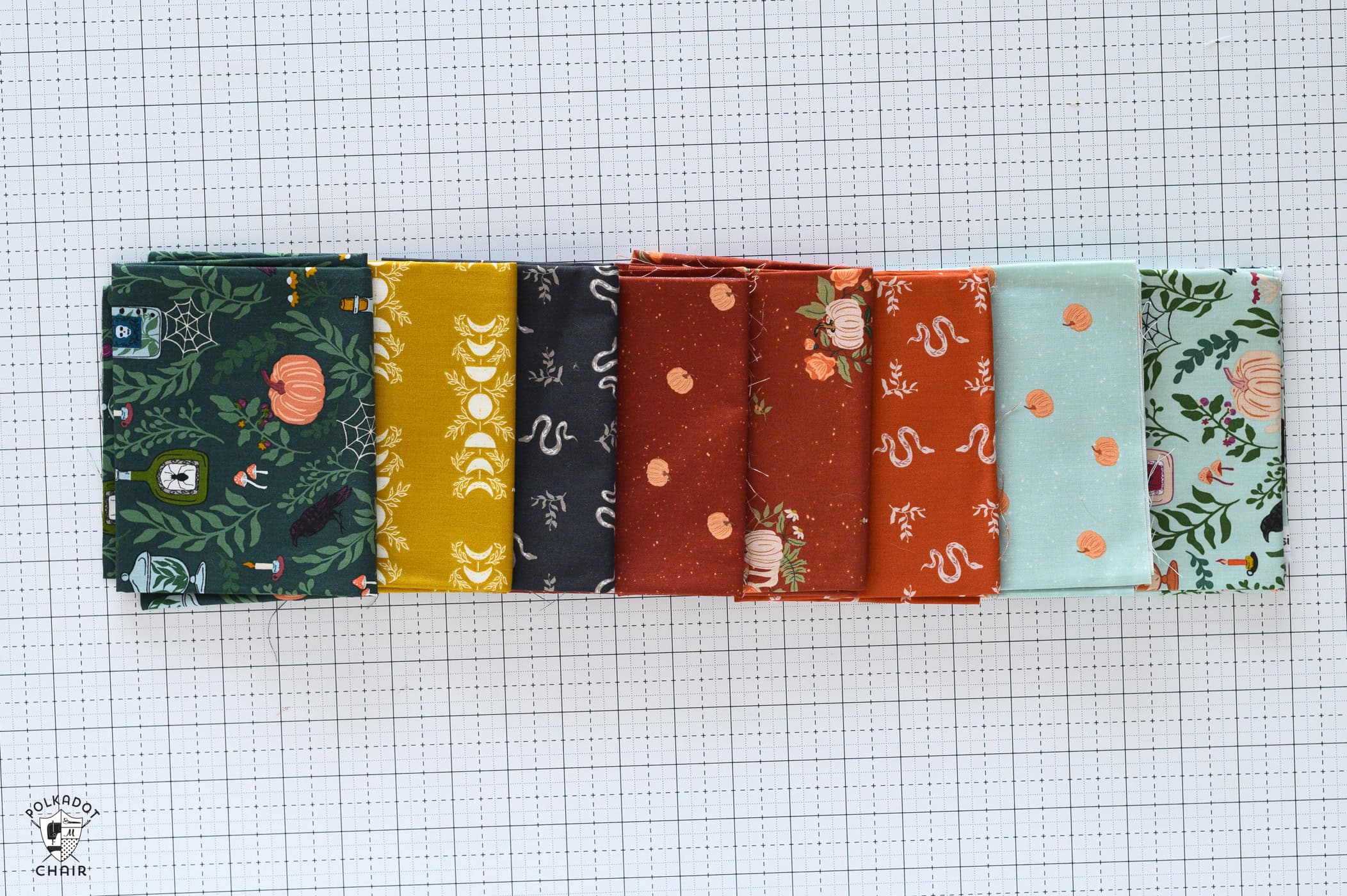 teal, yellow and burnt red fabric fat quarters folded on cutting mat