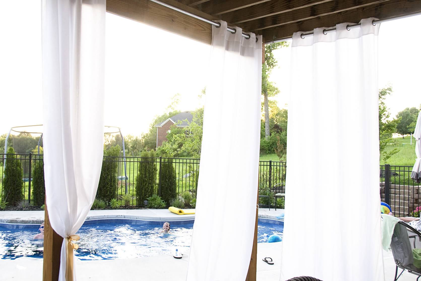 White drapes hanging from wood deck with pool in background