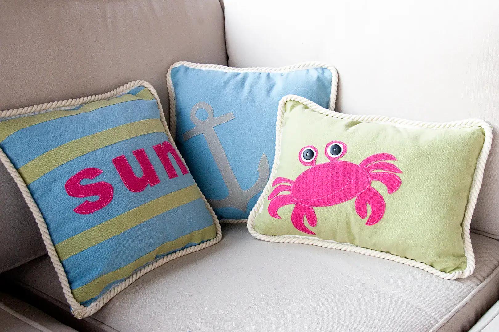 Three pillows on an outdoor couch, blue, green and green with a pink crab