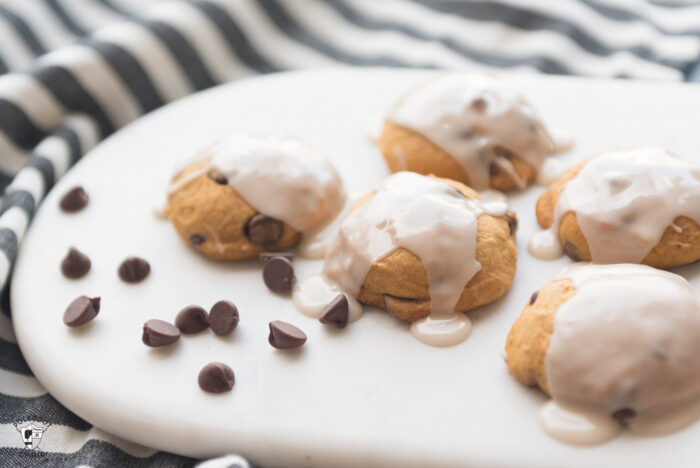 close up of pumpkin chocolate chip cookies on white marble cutting board with chocolate chips scattered on cutting board