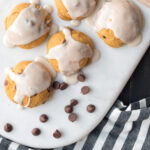 close up of pumpkin chocolate chip cookies on white marble cutting board with chocolate chips scattered on cutting board