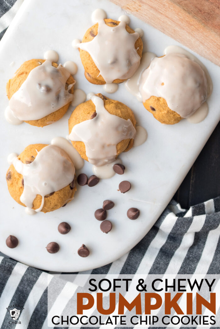 close up of pumpkin chocolate chip cookies on white marble cutting board with chocolate chips scattered on cutting board