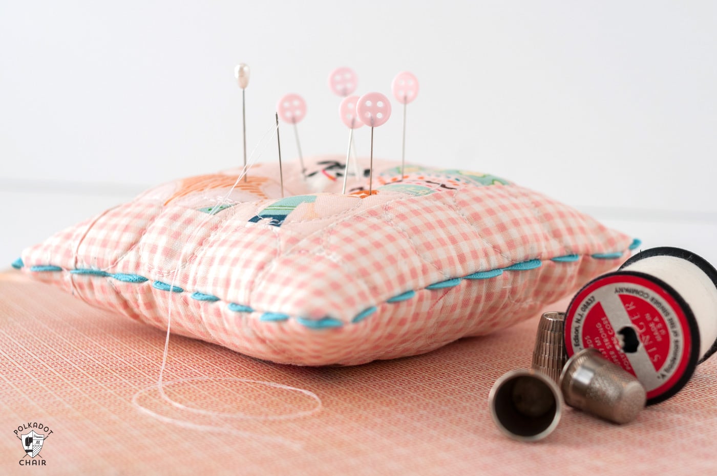 pink patchwork pincushion on gingham paper with sewing notions