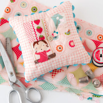 pink patchwork pincushion on white table with sewing notions