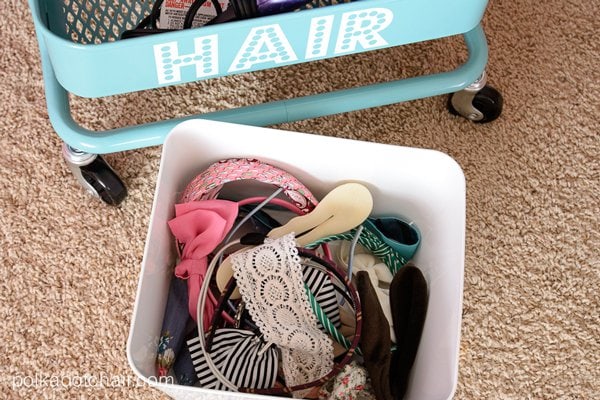 white bin filled with various hair accessories including headbands and hair bows on tan carpet. 