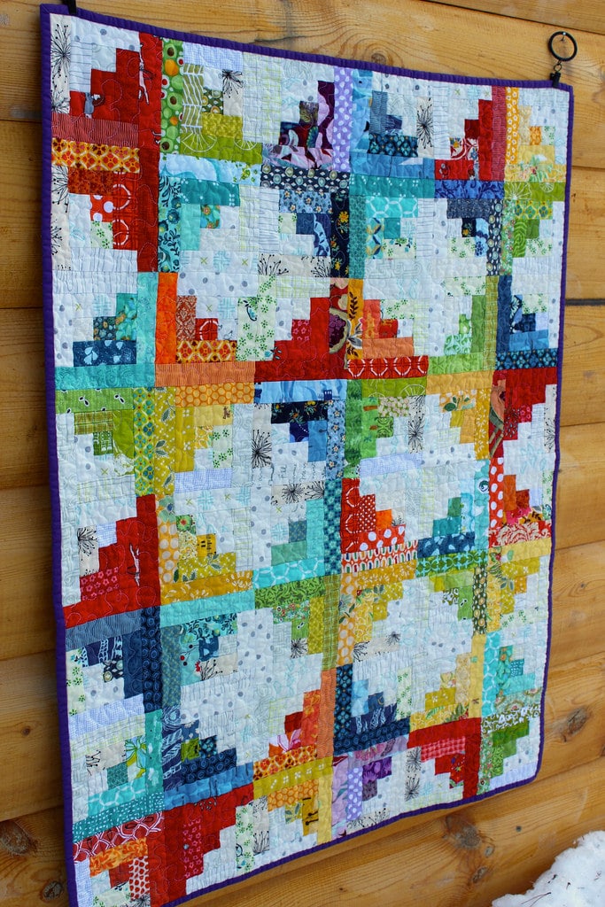 Multi color quilt hanging from a wooden wall.