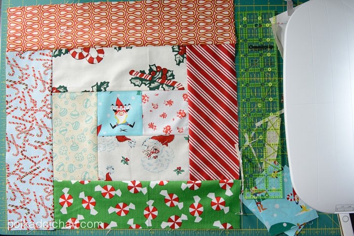 Christmas themed fabric sewn together on green cutting mat next to quilting ruler.