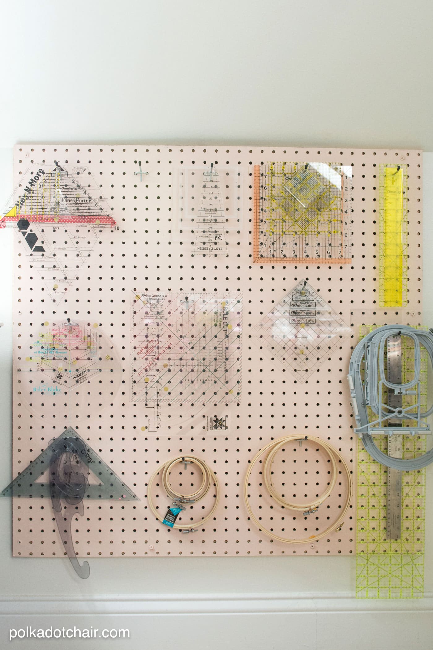 Pink pin board with rulers hanging on it on white wall