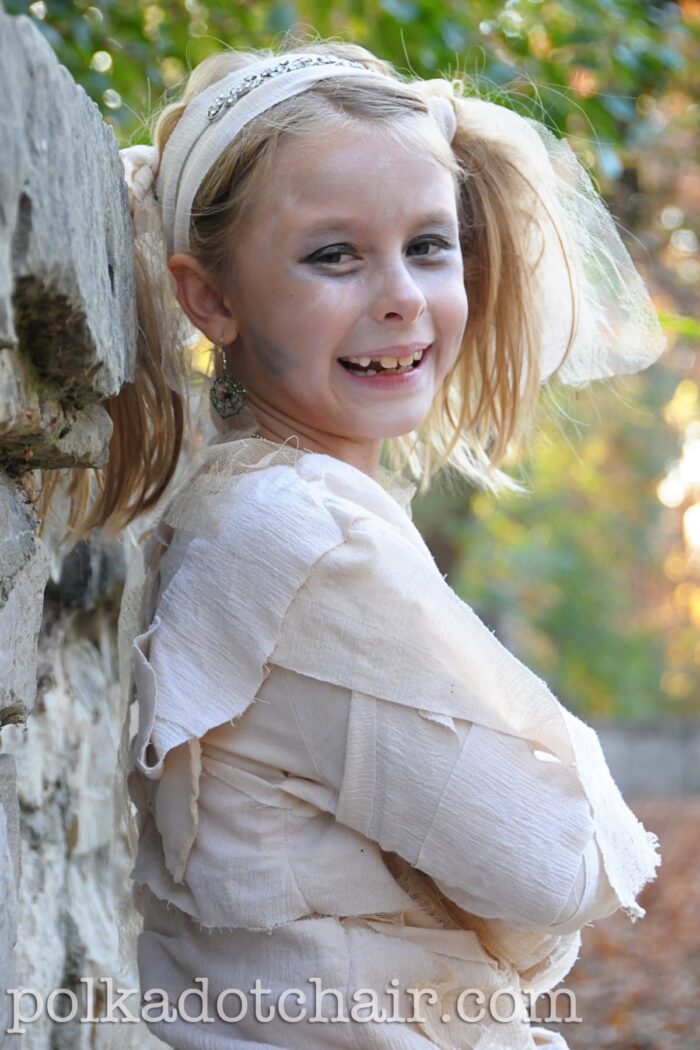 girl dressed up like mummy leaning on stone wall