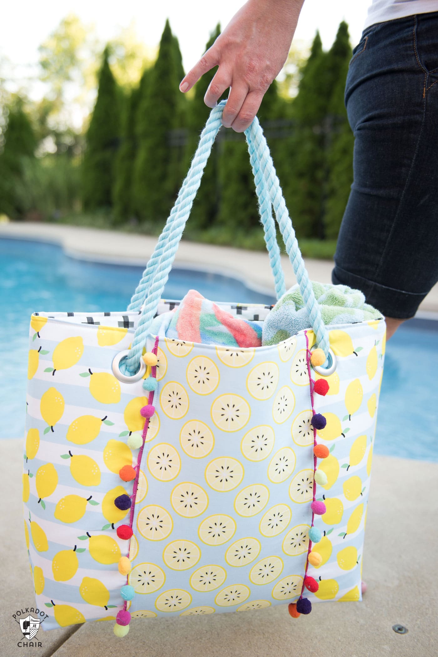 Person holding lemon themed beach bag in front of pool.