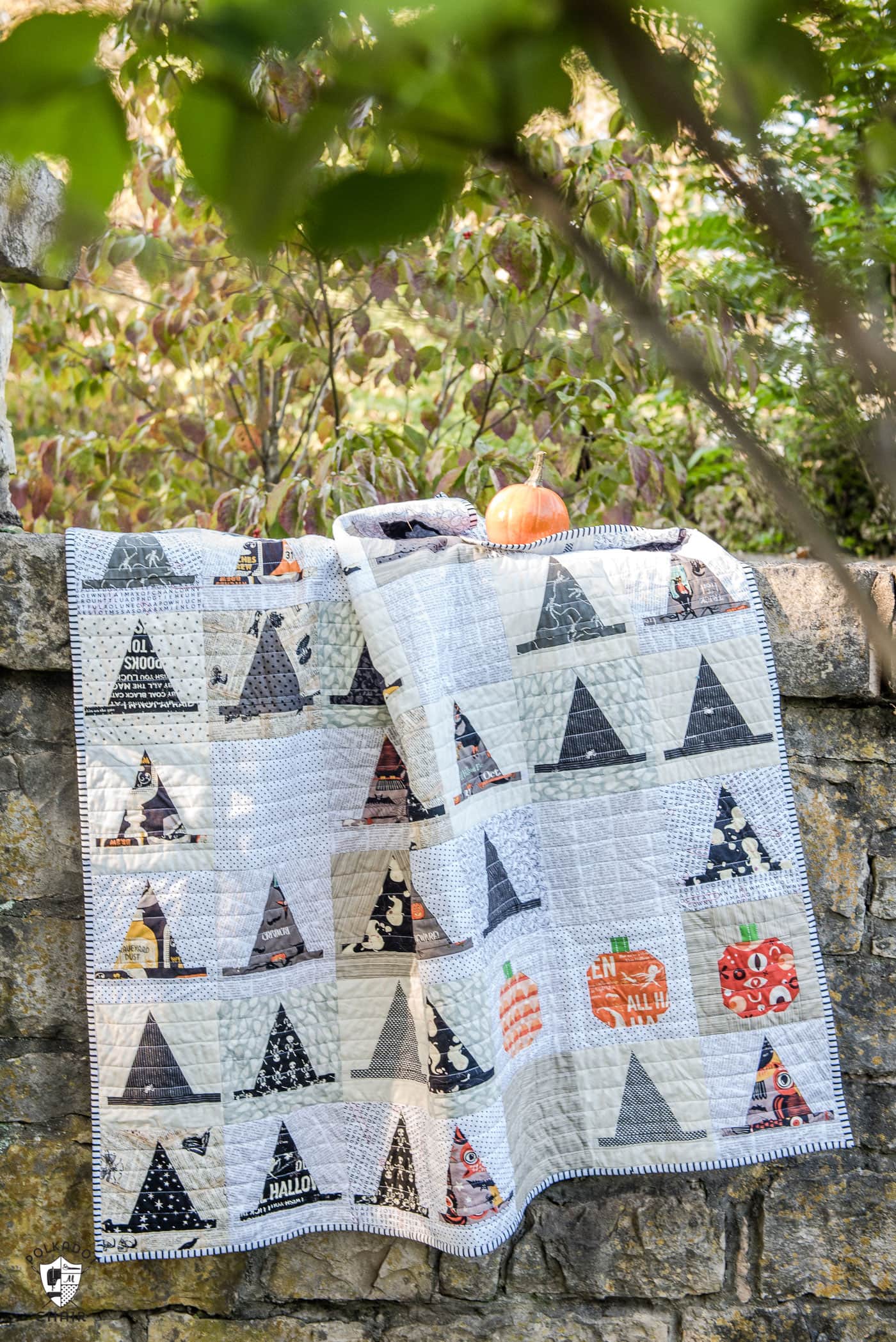 Halloween Haberdashery Quilt by Melissa Mortenson - a cute Witch's Hat Halloween Quilt pattern hanging on stone wall with pumpkin