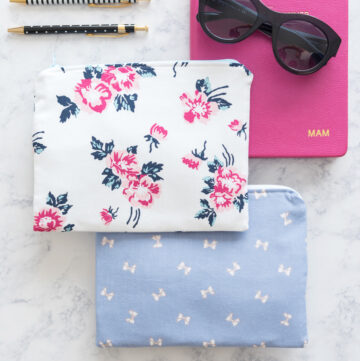 two zip pouches on white marble table with pink book and pens