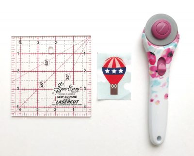 photo of quilt ruler, fabric and cutter on white table
