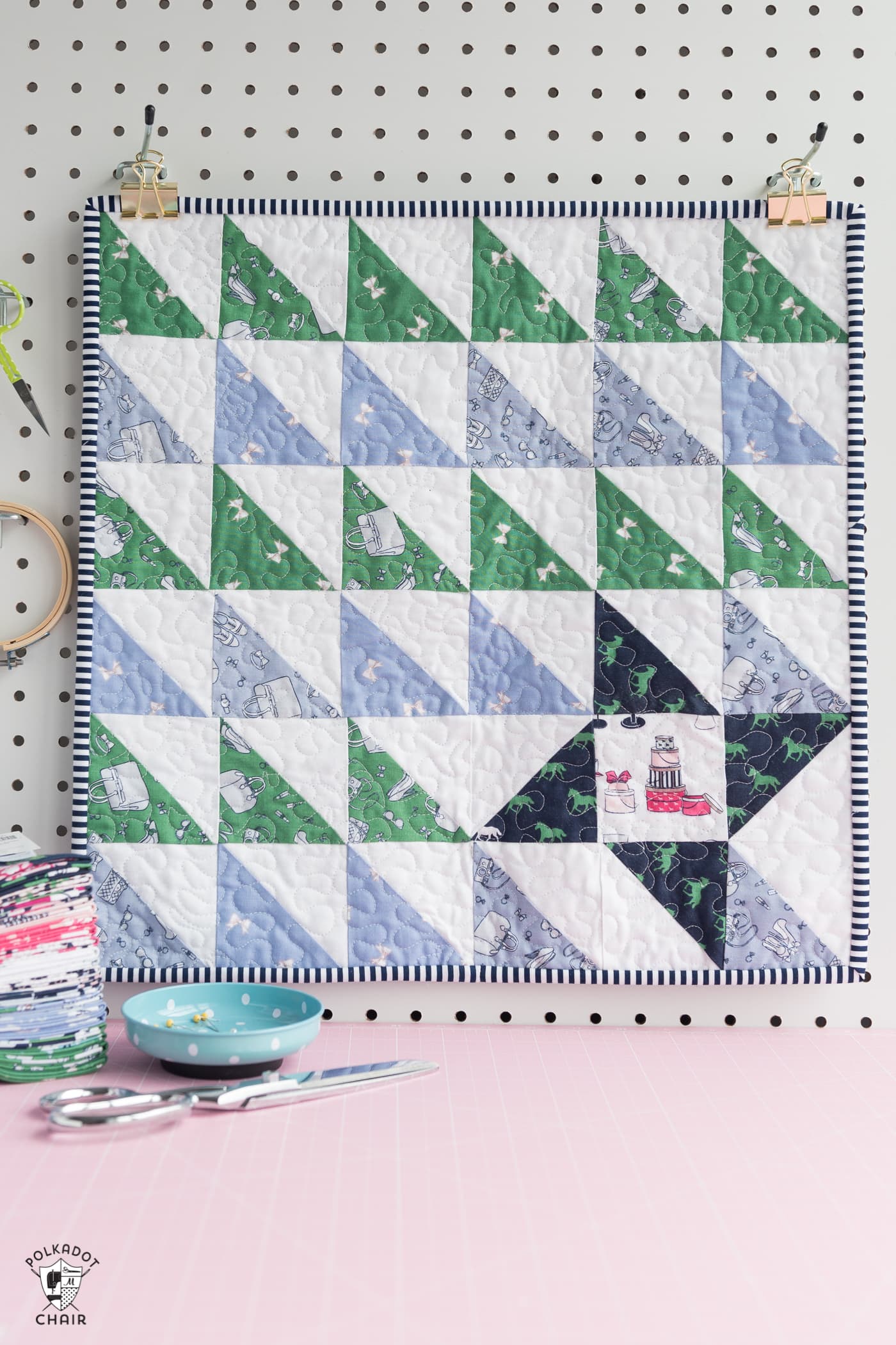 periwinkle, green and navy mini quilt hanging on peg board