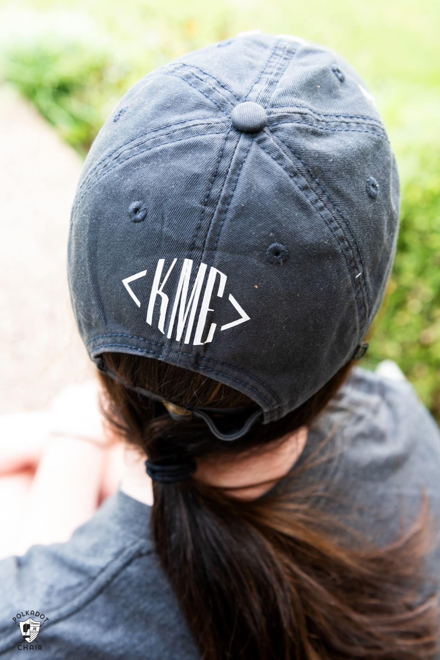 Back of girls head waring a navy baseball cap with white monogram "KME". 