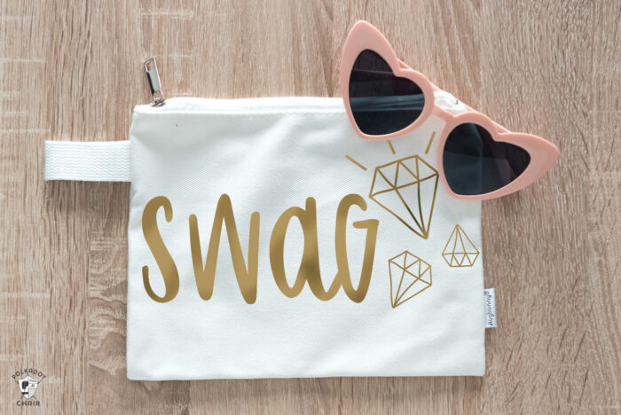 Swag Cricut SVG file cut out with gold iron on vinyl on white bag on tabletop with pink heart sunglasses