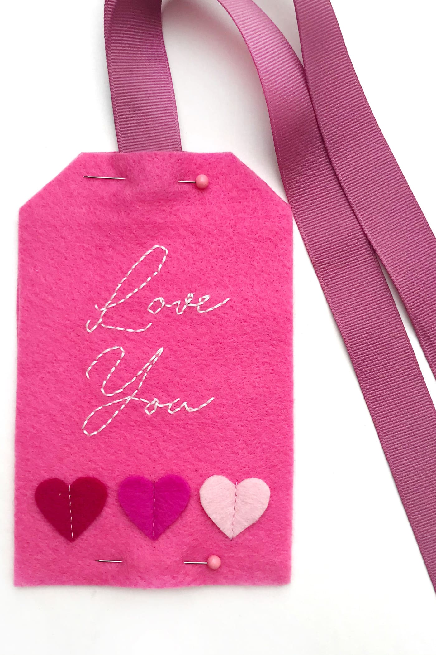 hand embroidered felt gift tags on white table showing ribbon attachment process