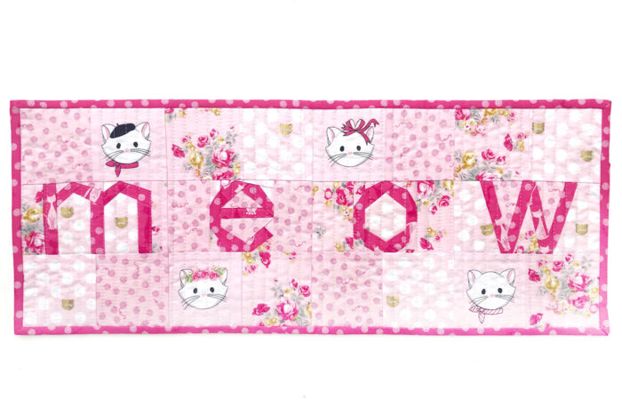 Pink and white MEOW quilted table runner on white tabletop