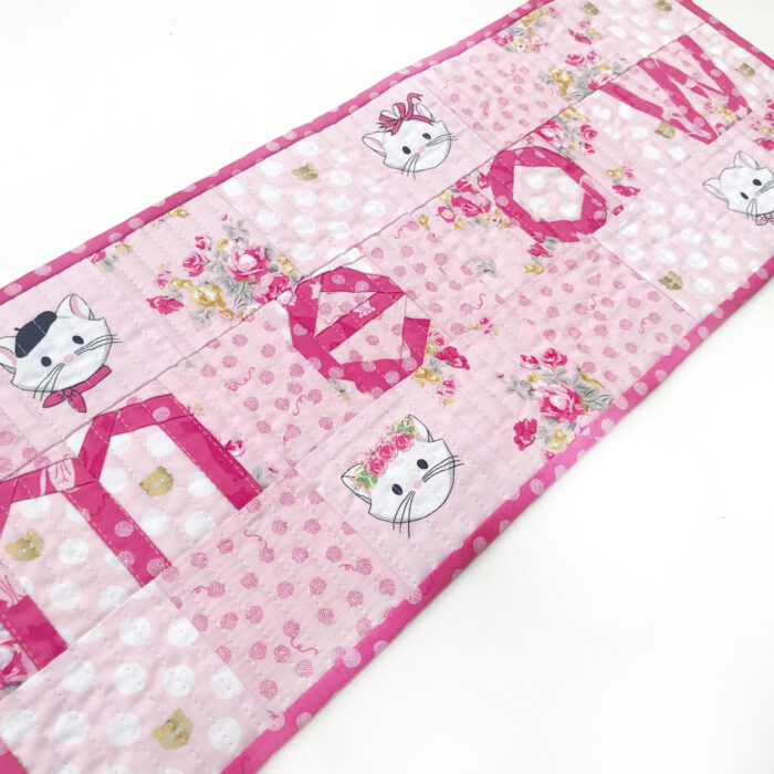 Pink and white MEOW quilted table runner on white tabletop