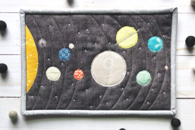 Colorful fabric Solar System mug rug on white wood table