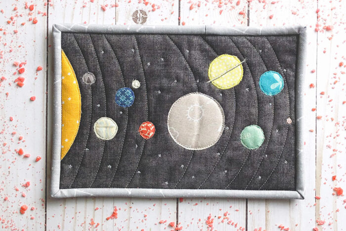 Colorful fabric Solar System mug rug on white wood table