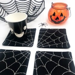 4 black and white spiderweb coasters on white table with halloween props