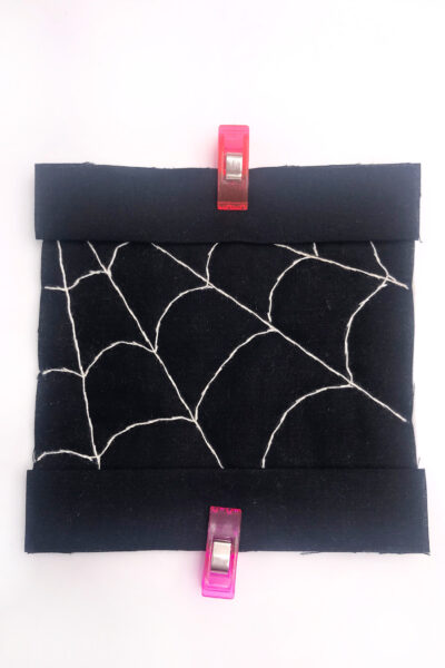 black fabric with a white spiderweb stitched with white thread on white table