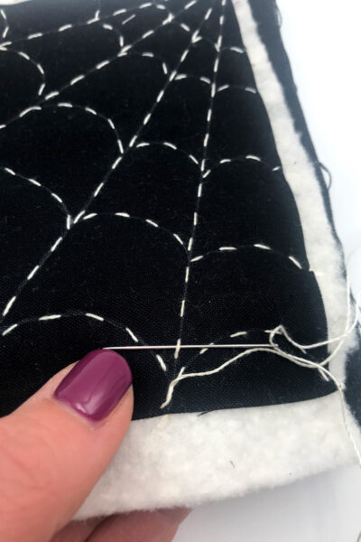 black fabric with a white spiderweb stitched with white thread on white table