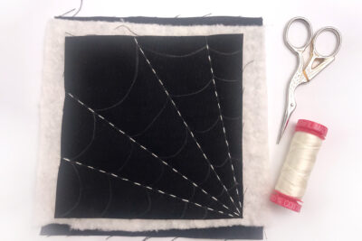 black fabric with a white spiderweb stitched with white thread on white table